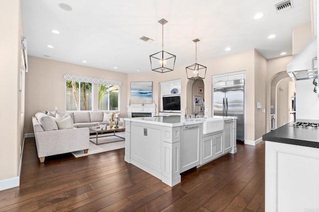 kitchen featuring a sink, arched walkways, built in fridge, visible vents, and dark wood-style floors