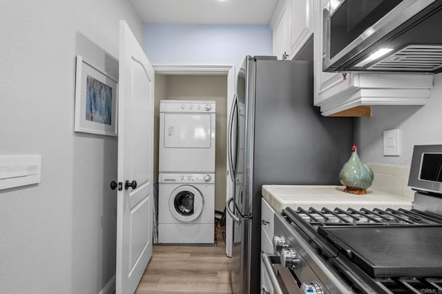 kitchen featuring stacked washer and clothes dryer, stainless steel gas range, tile counters, white cabinets, and light wood-style flooring