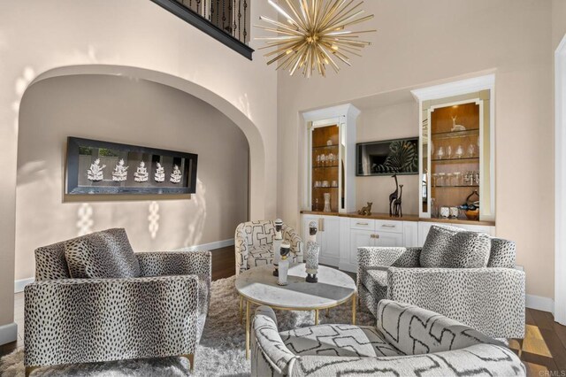 sitting room featuring wood finished floors, baseboards, a chandelier, arched walkways, and bar area