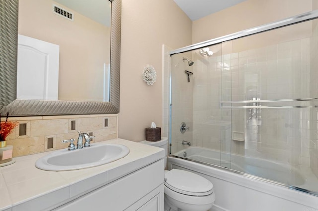 full bathroom featuring visible vents, vanity, toilet, shower / bath combination with glass door, and tasteful backsplash