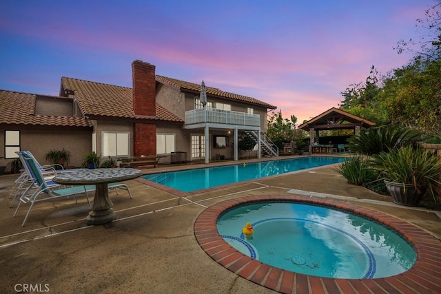 pool at dusk featuring an in ground hot tub, a patio area, and a gazebo