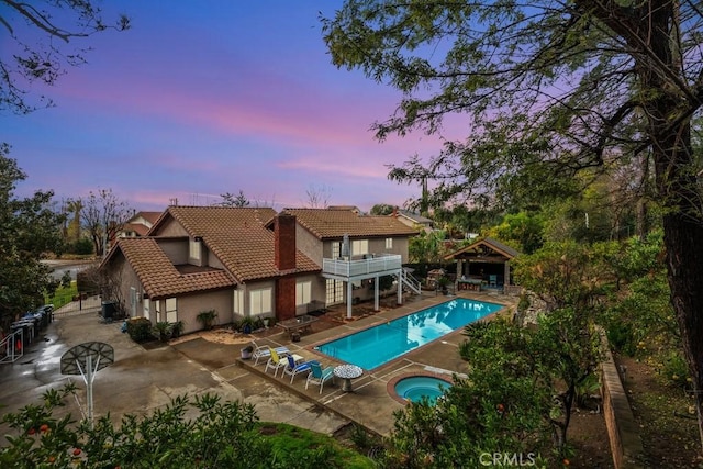 pool at dusk featuring a patio and an in ground hot tub