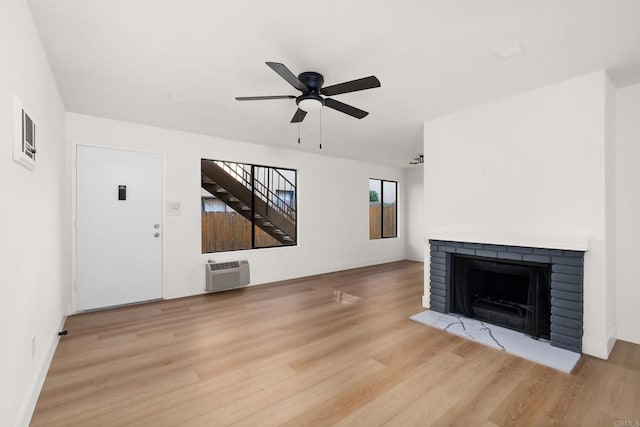 unfurnished living room featuring a brick fireplace, light hardwood / wood-style flooring, an AC wall unit, and ceiling fan