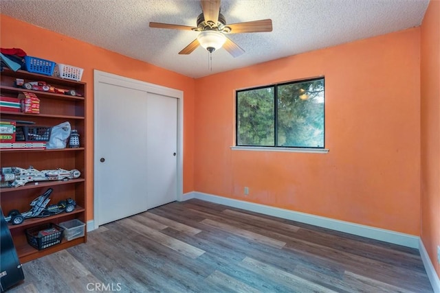 unfurnished bedroom with wood-type flooring, ceiling fan, a textured ceiling, and a closet