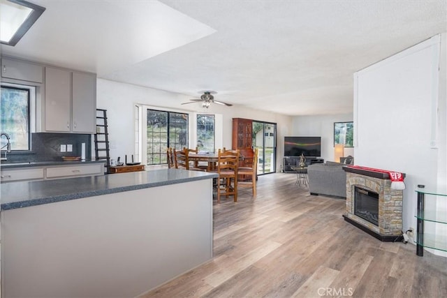 kitchen featuring gray cabinetry, a stone fireplace, light hardwood / wood-style floors, and ceiling fan