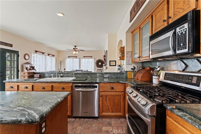 kitchen featuring sink, appliances with stainless steel finishes, ceiling fan, dark stone counters, and decorative backsplash