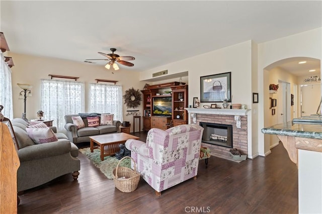 living room featuring ceiling fan, dark hardwood / wood-style flooring, and a brick fireplace