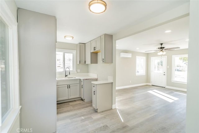 kitchen featuring sink, a wall mounted air conditioner, ceiling fan, and light hardwood / wood-style flooring