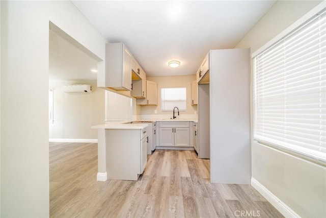 kitchen with sink, a wall mounted air conditioner, white cabinets, and light hardwood / wood-style flooring