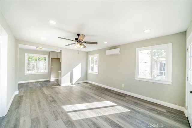 empty room featuring a wall unit AC, light hardwood / wood-style floors, and ceiling fan