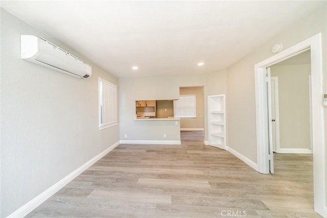 unfurnished living room featuring a wall mounted AC and light hardwood / wood-style flooring