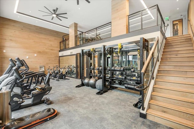 gym with ceiling fan, a high ceiling, and wood walls