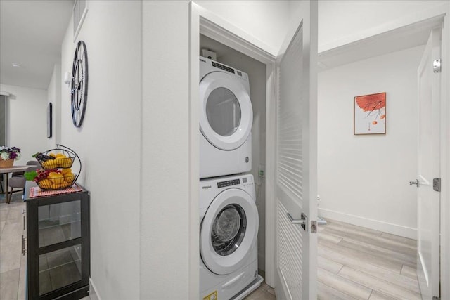 clothes washing area featuring stacked washing maching and dryer and light hardwood / wood-style floors