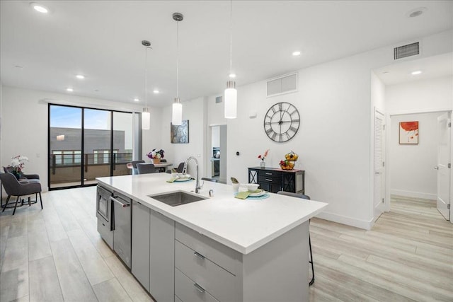 kitchen with decorative light fixtures, sink, gray cabinetry, a kitchen island with sink, and light hardwood / wood-style floors