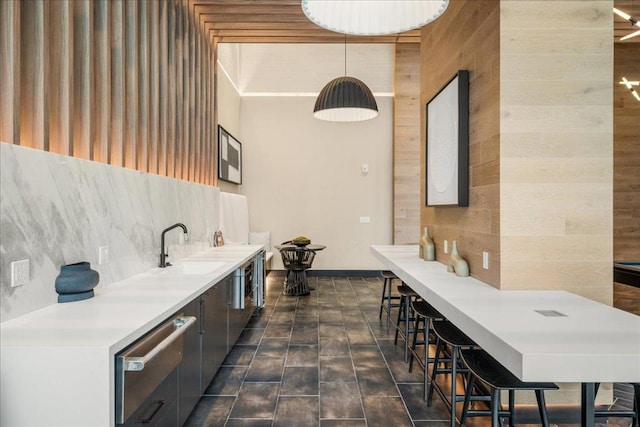 bar with hanging light fixtures, tasteful backsplash, sink, and wood walls