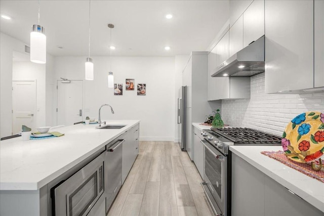 kitchen featuring sink, wall chimney range hood, high end appliances, tasteful backsplash, and decorative light fixtures