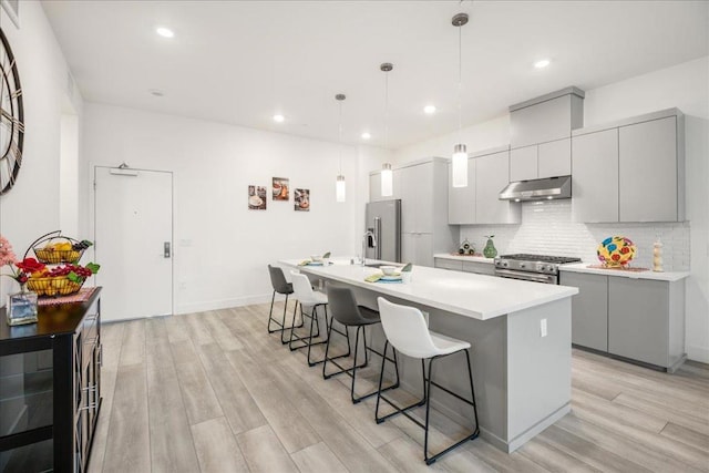 kitchen with gray cabinets, a breakfast bar, pendant lighting, high quality appliances, and backsplash