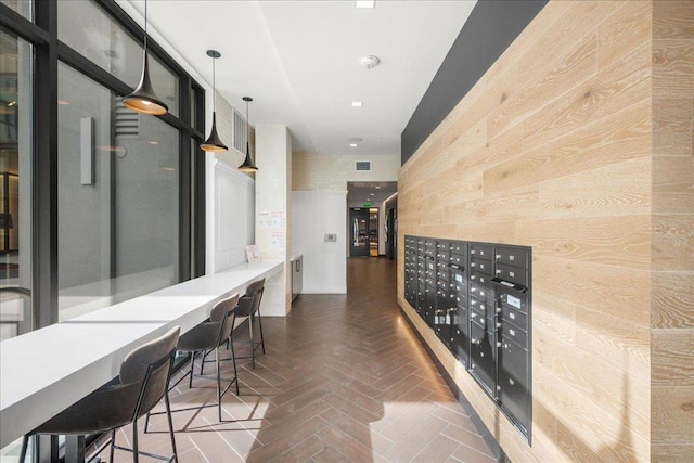 hallway with dark parquet flooring, wooden walls, and a mail area