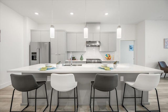 kitchen with a kitchen island with sink, decorative backsplash, light hardwood / wood-style flooring, and appliances with stainless steel finishes