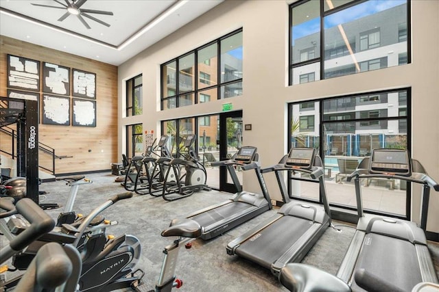 exercise room with ceiling fan, wooden walls, a healthy amount of sunlight, and a high ceiling