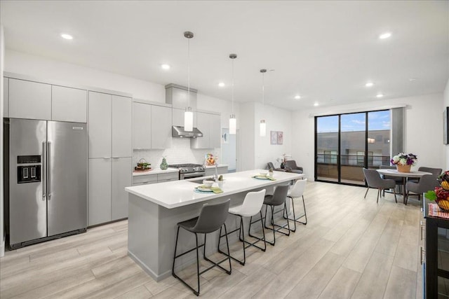 kitchen featuring tasteful backsplash, decorative light fixtures, appliances with stainless steel finishes, a kitchen island with sink, and white cabinets