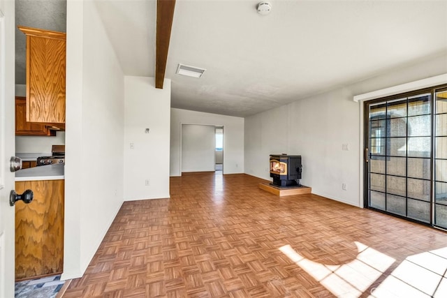 unfurnished living room with beam ceiling, a wood stove, and light parquet floors