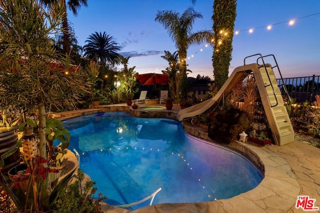 pool at dusk with an in ground hot tub, a water slide, and a patio