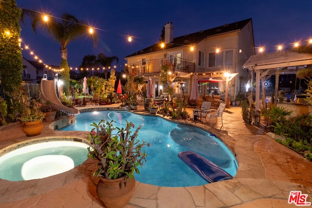 pool at twilight with an in ground hot tub, a water slide, and a patio area