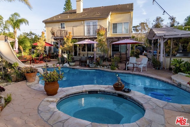 back of house featuring a swimming pool with hot tub, a patio, and a balcony