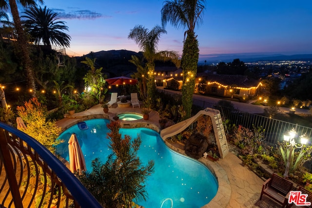 pool at dusk featuring an in ground hot tub, a water slide, and a patio area