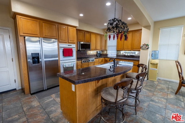 kitchen featuring an island with sink, appliances with stainless steel finishes, sink, and backsplash