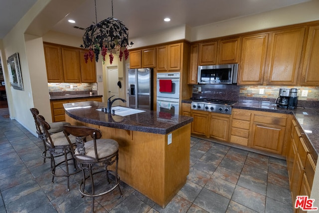 kitchen with a breakfast bar, sink, stainless steel appliances, a kitchen island with sink, and backsplash