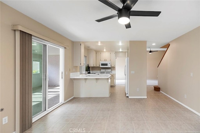 kitchen featuring a kitchen bar, sink, kitchen peninsula, ceiling fan, and stove