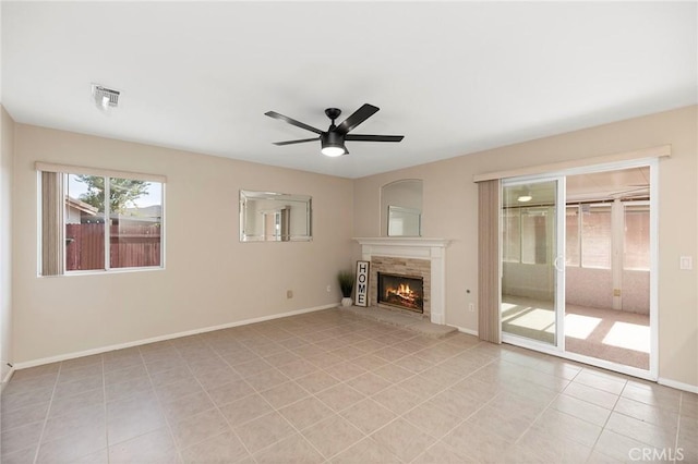 unfurnished living room with a stone fireplace, ceiling fan, and light tile patterned flooring