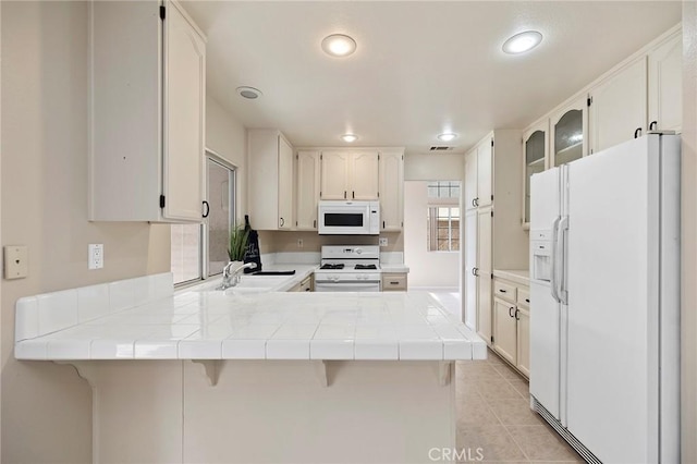 kitchen featuring white cabinetry, white appliances, a breakfast bar area, and kitchen peninsula