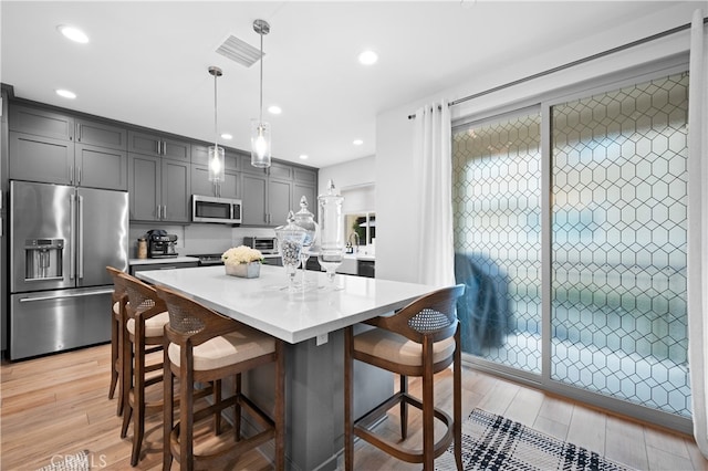 kitchen featuring gray cabinetry, a kitchen breakfast bar, hanging light fixtures, stainless steel appliances, and light wood-type flooring