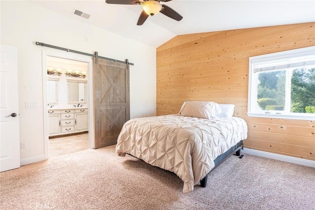 bedroom with vaulted ceiling, ensuite bathroom, wood walls, a barn door, and light carpet