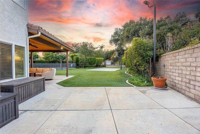 patio terrace at dusk featuring an outdoor living space, ceiling fan, and a lawn