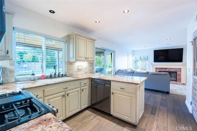 kitchen featuring black dishwasher, sink, kitchen peninsula, cream cabinets, and light wood-type flooring