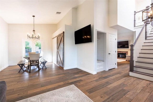 dining area featuring a barn door, dark wood-type flooring, a chandelier, and a towering ceiling