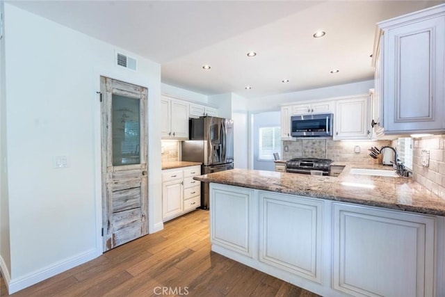 kitchen with appliances with stainless steel finishes, sink, white cabinets, and kitchen peninsula