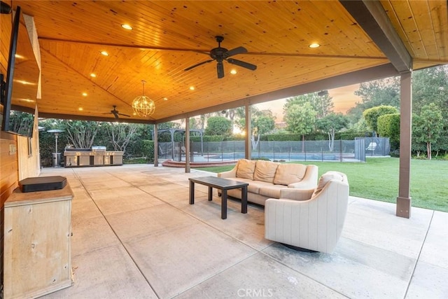 patio terrace at dusk with a lawn, outdoor lounge area, ceiling fan, and an outdoor kitchen