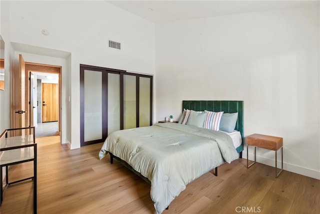 bedroom with a towering ceiling, light hardwood / wood-style floors, and a closet