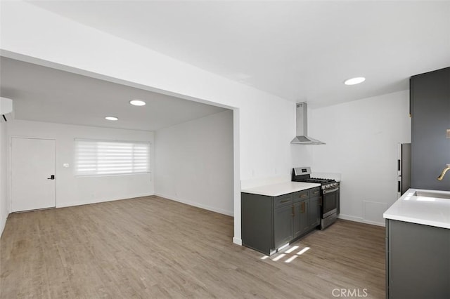 kitchen with sink, light hardwood / wood-style flooring, stainless steel gas stove, an AC wall unit, and wall chimney exhaust hood