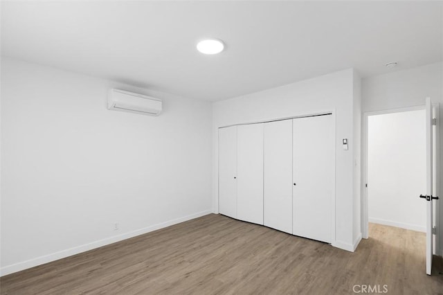 unfurnished bedroom with a closet, an AC wall unit, and light hardwood / wood-style flooring