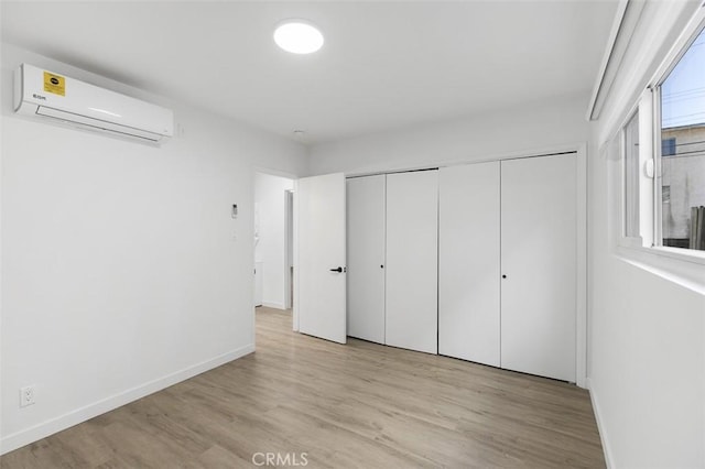 unfurnished bedroom featuring light wood-type flooring and an AC wall unit