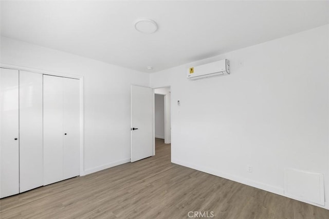 unfurnished bedroom featuring a closet, light hardwood / wood-style floors, and an AC wall unit