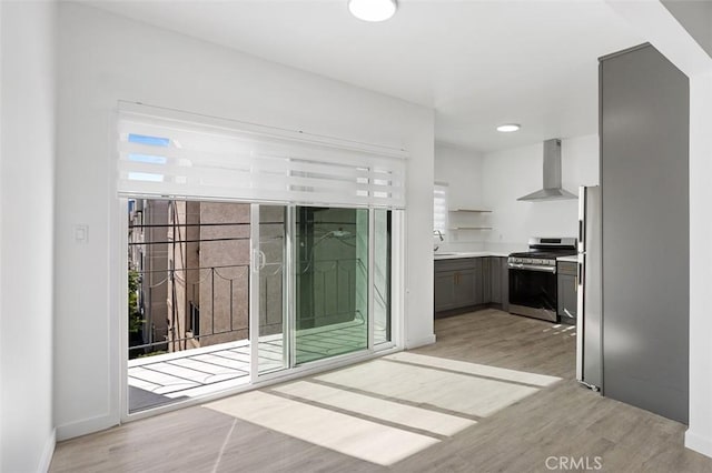 interior space with sink, wall chimney range hood, stainless steel stove, and light wood-type flooring