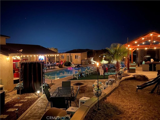 pool at night with a fire pit and a patio