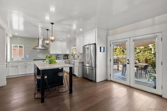 kitchen with high end fridge, white cabinets, pendant lighting, and wall chimney exhaust hood